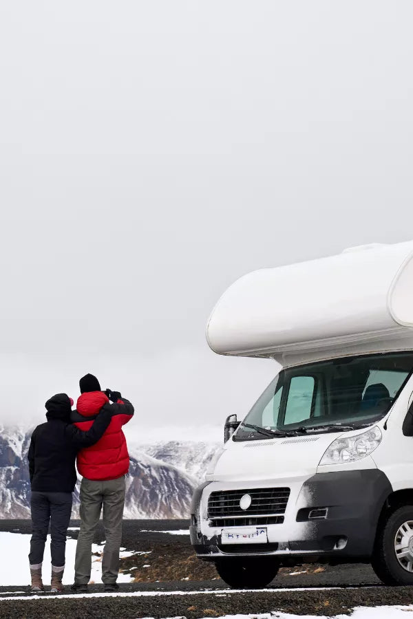 Two people embracing in front of a white camper van with mountains