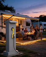 Group of people gathered around a dining table outside an RV at dusk, with a charging station 